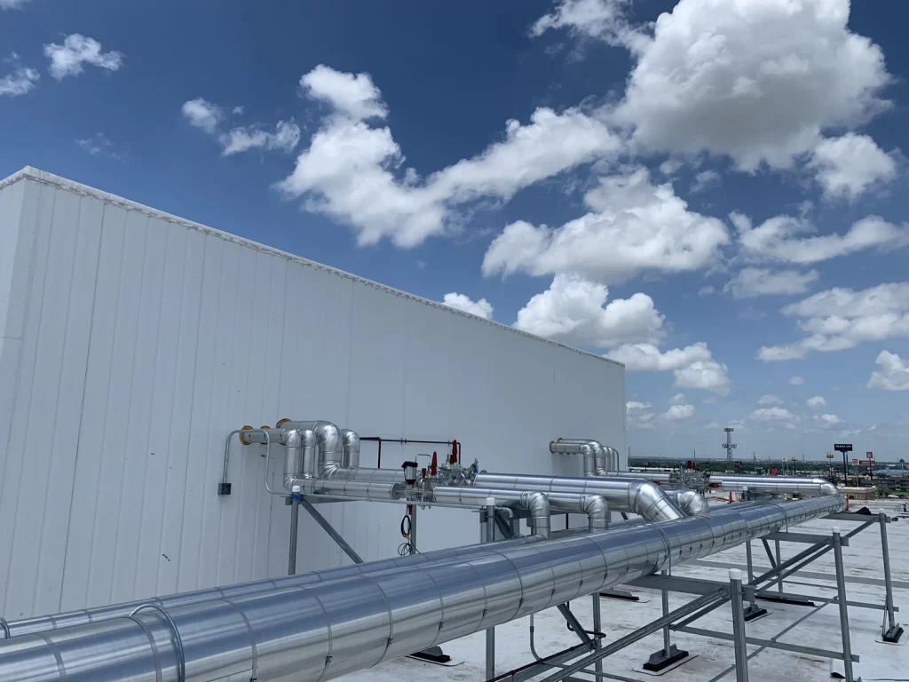 Outdoor industrial piping system atop a building with a cloudy sky overhead.