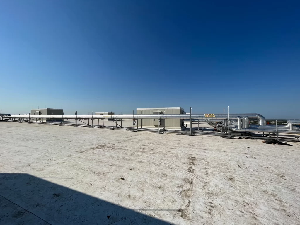 A flat, expansive rooftop with HVAC systems, metal ductwork, and industrial equipment under a clear blue sky.