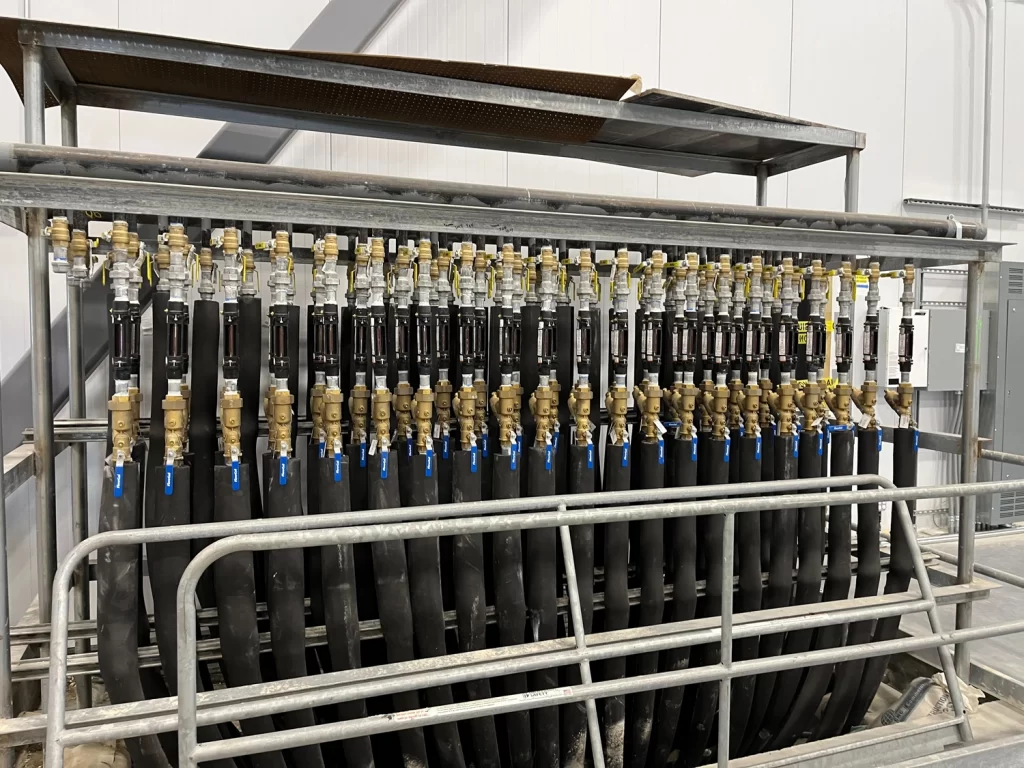 A metal rack holds multiple black hoses connected to a series of yellow-handled valves in an industrial facility.