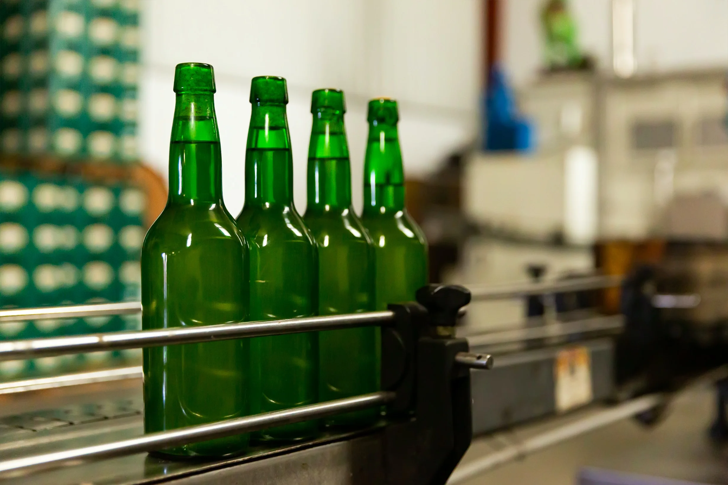 Four green glass bottles on a conveyor belt in a factory setting.