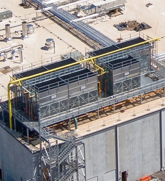 A rooftop view of an industrial facility showing large cooling units, pipes, and metal structures.