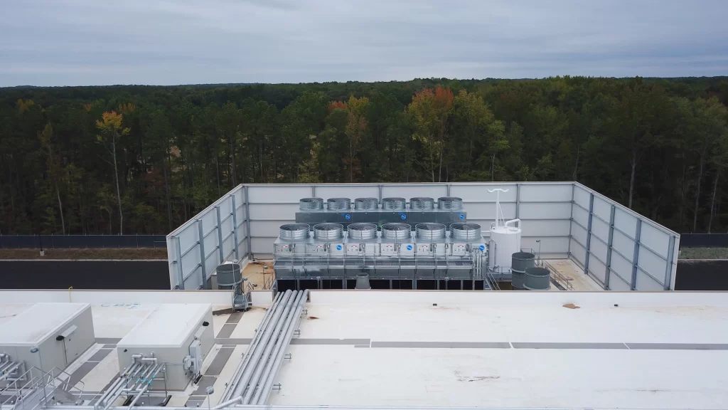 Rooftop view of an industrial facility surrounded by a forest, featuring multiple large cylindrical structures and piping systems.