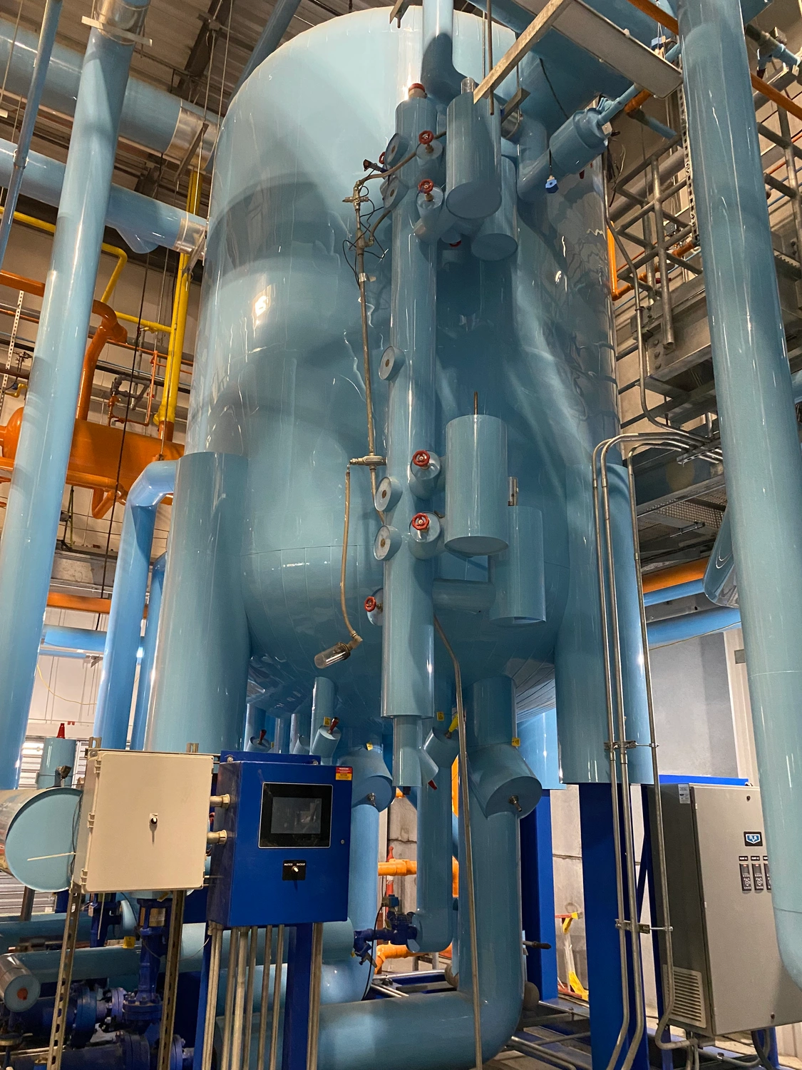 A large industrial boiler in a facility with various pipes, gauges, and control panels. The equipment is mostly blue and appears to be part of a complex mechanical system.