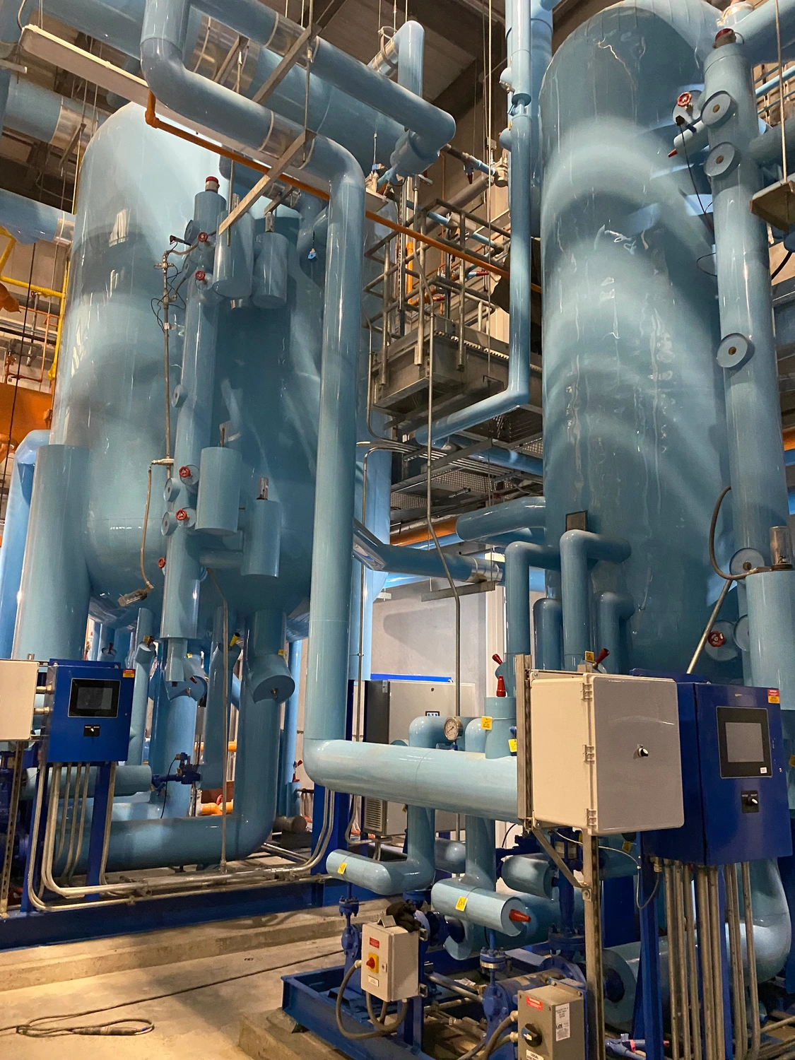 A large industrial facility with tall blue tanks, various pipes, and control panels.